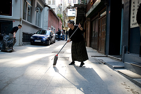 Eine alte Frau fegt die Strasse vor einem Hauseingang - Janet Große Fotografin Streetphotography